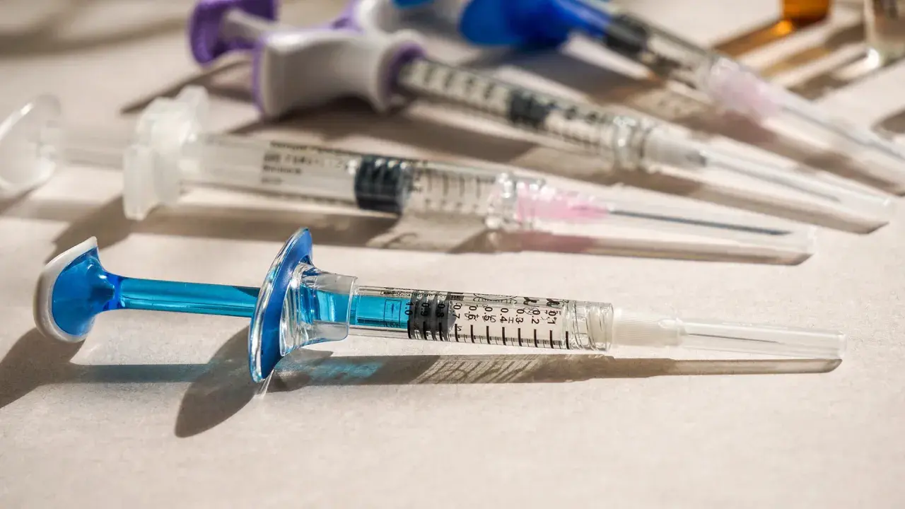 Flera sprutor med blå och lila detaljer ligger på en ljus yta. En spruta med blå kolv är i förgrunden, redo för vaccin i Colombia.