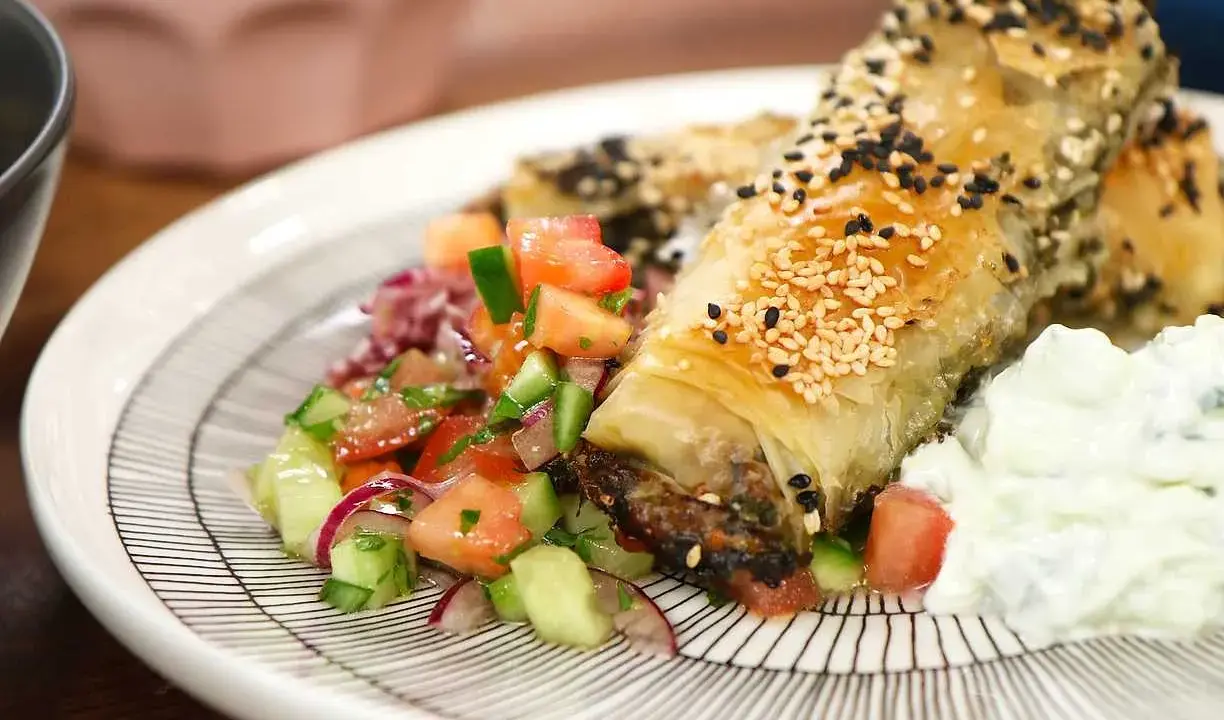 Krispiga filodegsrullar med sesamfrön, serverade med en fräsch tomatsallad och vitlökssås. Ett utsökt burek recept!