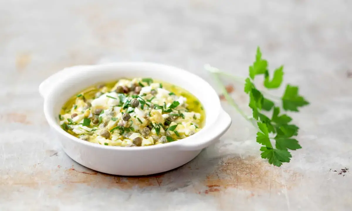 Sauce gribiche, une préparation maison à base d'œufs durs hachés, de câpres et de persil frais, dans un bol blanc.