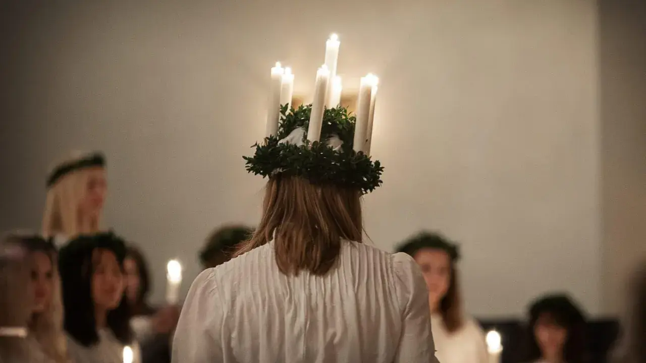 En flicka med ljuskrona bär fram ett lucia namn. Hon leder en procession av flickor med ljus i mörkret.