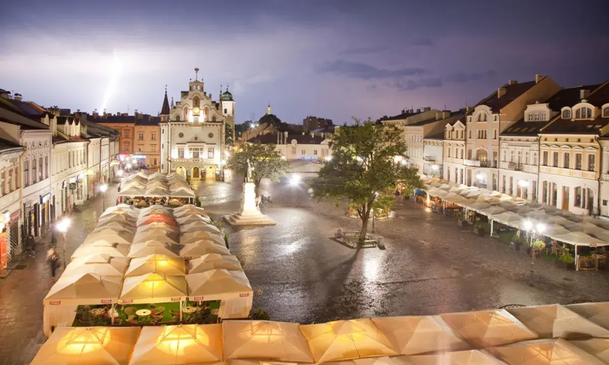 Nocny rzeszów rynek podczas burzy z piorunami. Mokry bruk, oświetlone kamienice i ogródki restauracyjne pod namiotami tworzą magiczny klimat.
