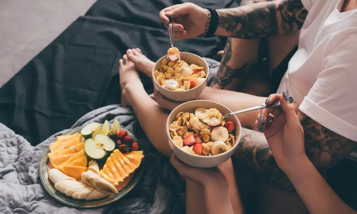 Para jedząca płatki z owocami i talerz świeżych owoców na łóżku. Zdrowy początek dnia, czyli zbilansowana dieta.