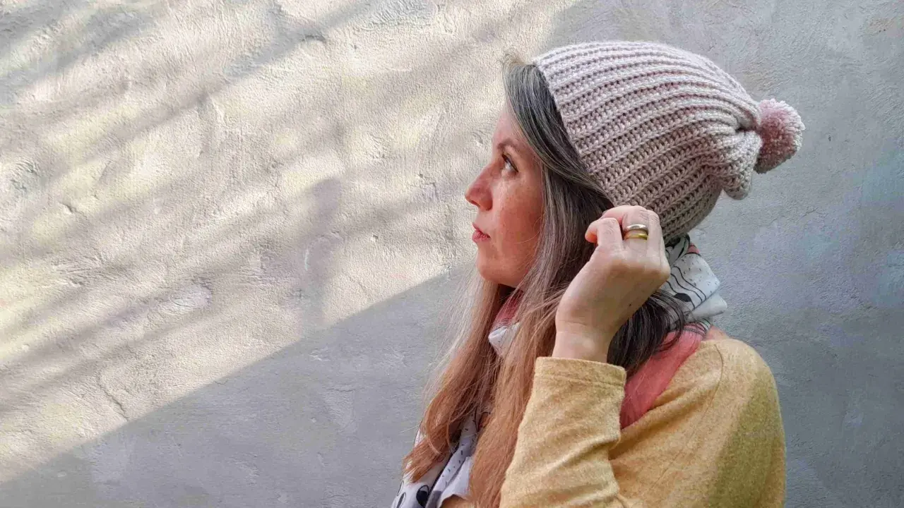 Mujer con gorro tejido a crochet, con pompón rosa. Disfruta del proceso de tejer gorros crochet.