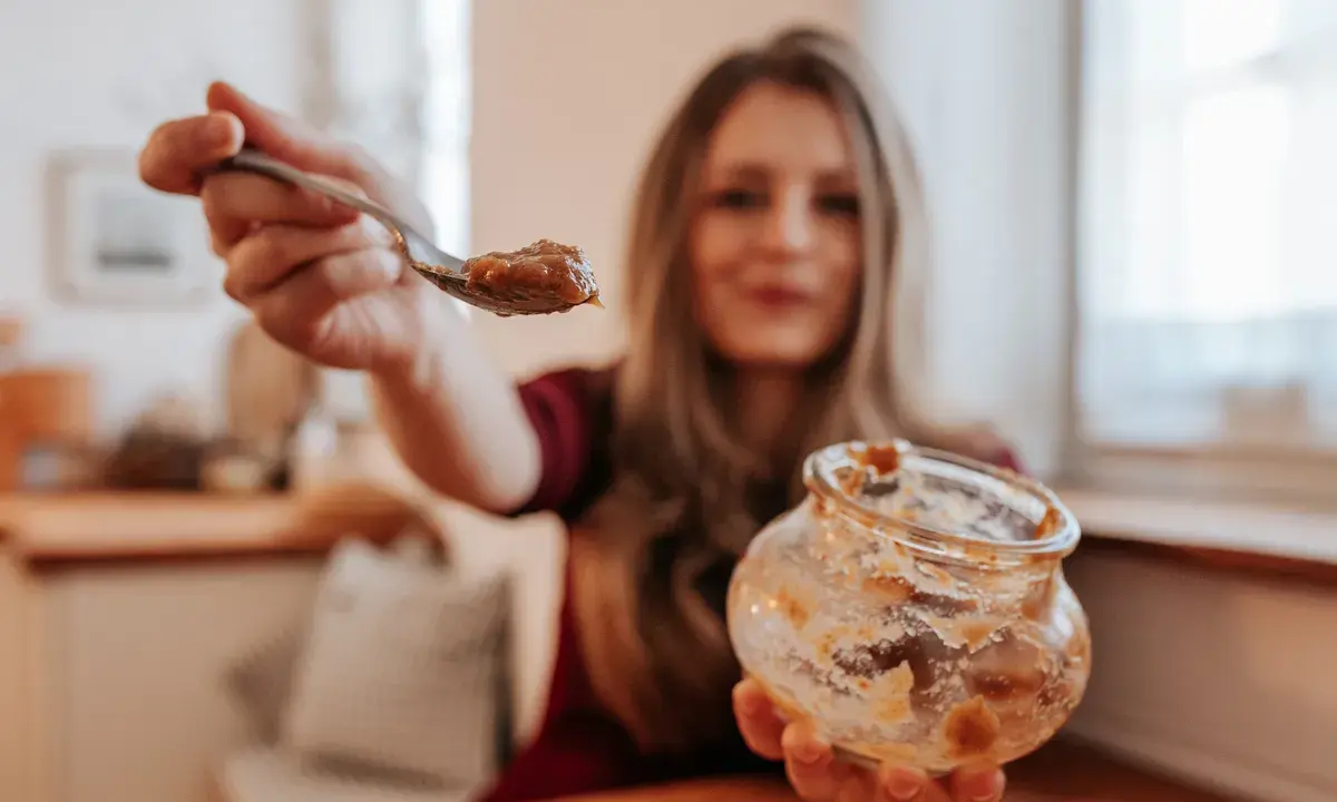 Frau mit Löffel und leerem Glas Apfelmus. Ein kleiner Fehler beim Einkochen, aber lecker!