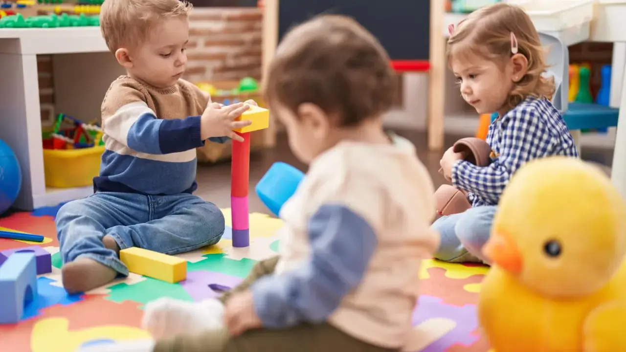 Trójka małych dzieci bawi się klockami i zabawkami na kolorowej macie w żłobku.