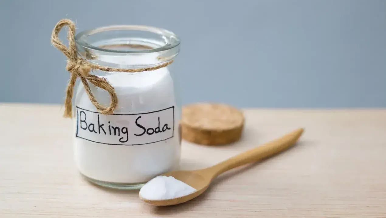 Słoik z napisem "Baking Soda" i drewniana łyżka z proszkiem. To naturalny sposób na usuwanie plam.
