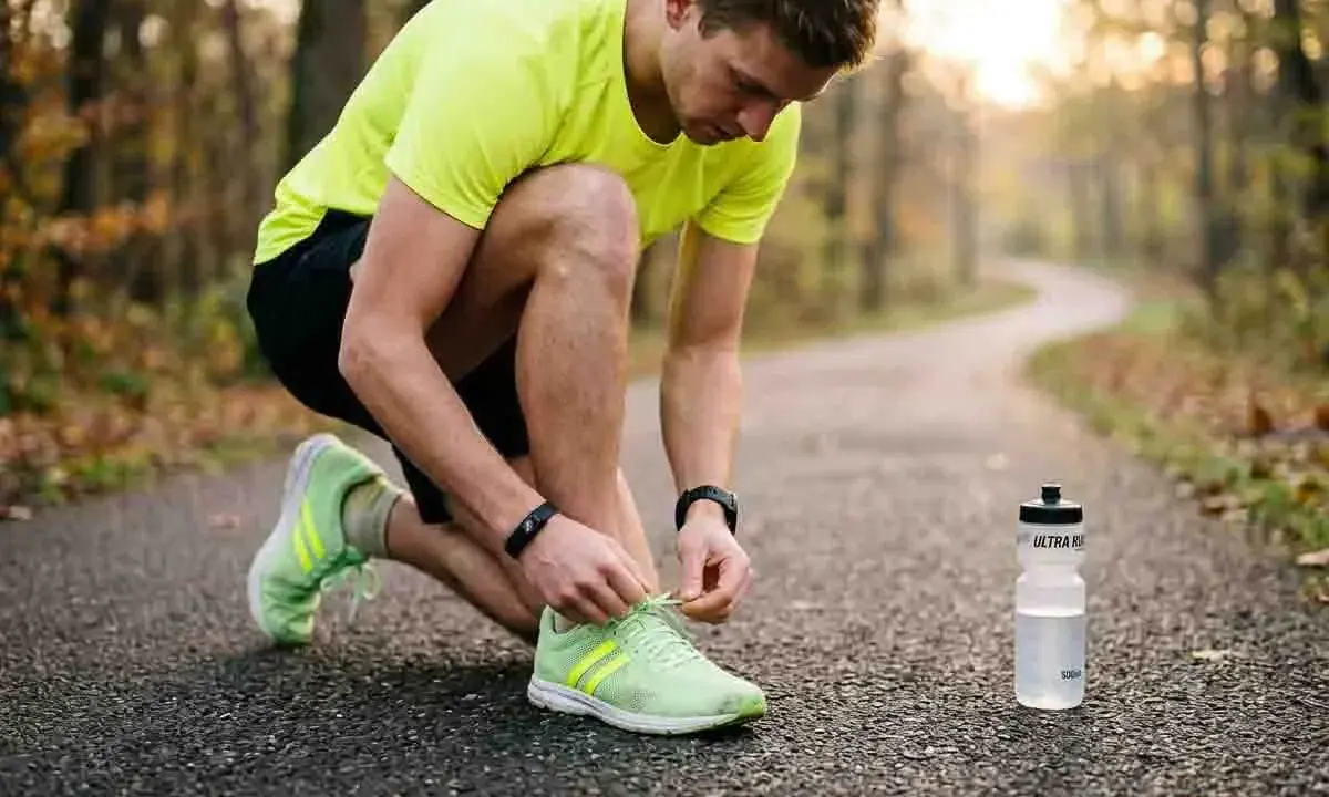 Ein Mann bindet sich die Schnürsenkel seiner Laufschuhe, bereit für eine Runde morgens oder abends joggen im Herbstwald.