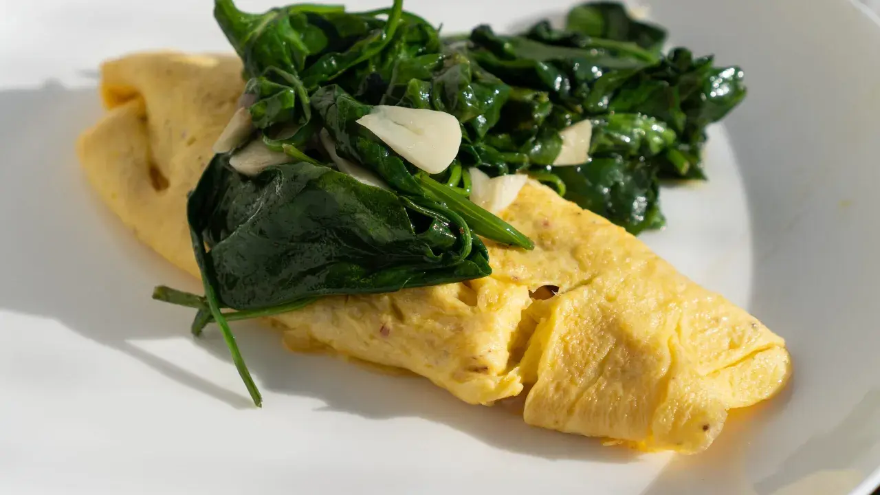 Złożony omlet francuski z zielonym szpinakiem i czosnkiem na białym talerzu.