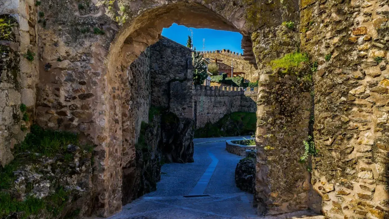 Un arco de piedra revela un camino empedrado y murallas, evocando la atmósfera de pueblos medievales cerca de Madrid.