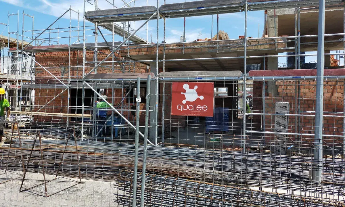 Obra en construcción con andamios y ladrillos. Se ve el logo de "qualee". ¿Cuánto se tarda en construir un edificio de 7 plantas?