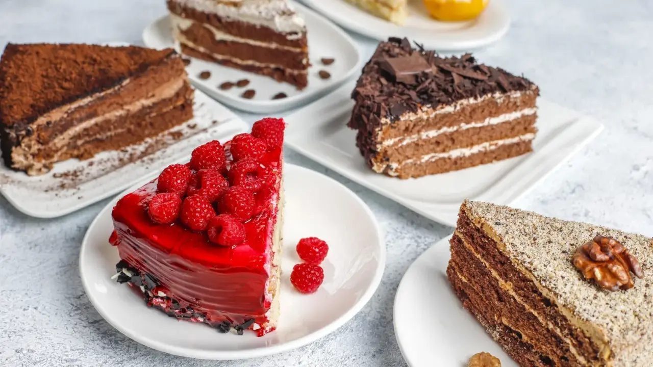 Variedad de pasteles en una mesa: uno de chocolate con cacao, otro con glaseado rojo y frambuesas, y uno con nueces. Una deliciosa carta de postres.