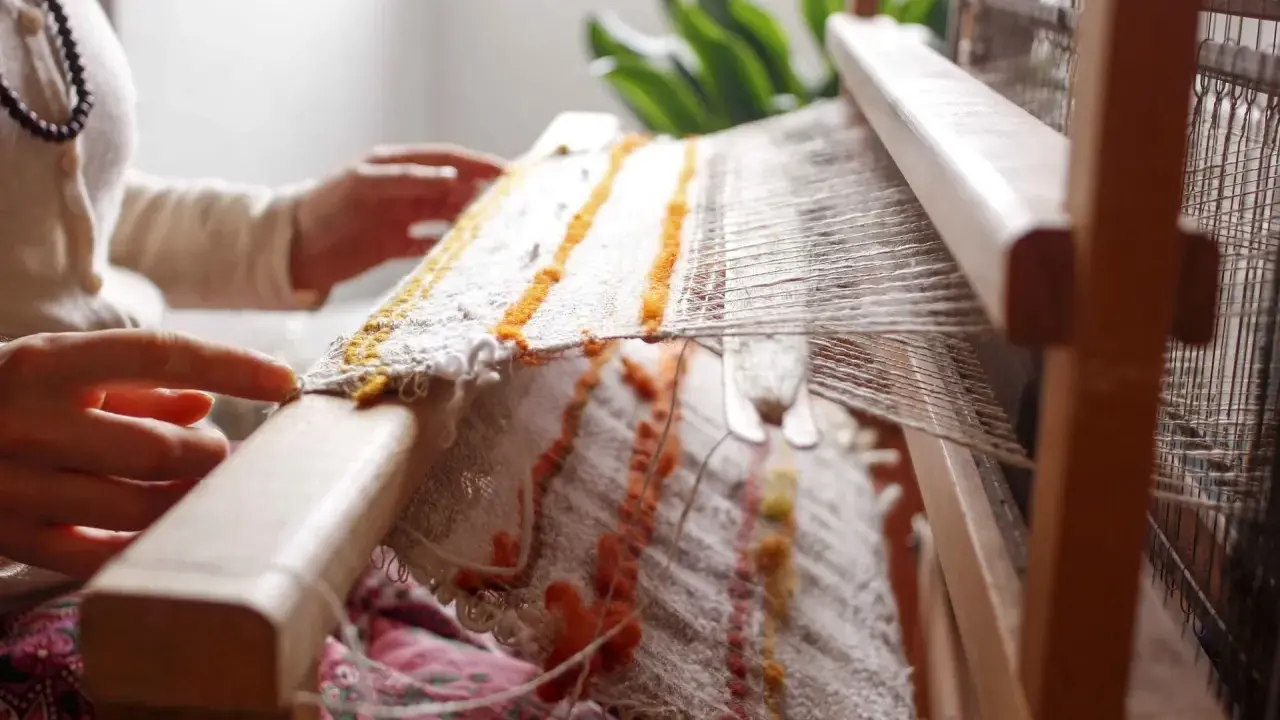 Hands weave a textured fabric on a loom, a beautiful example of textile upcycling.