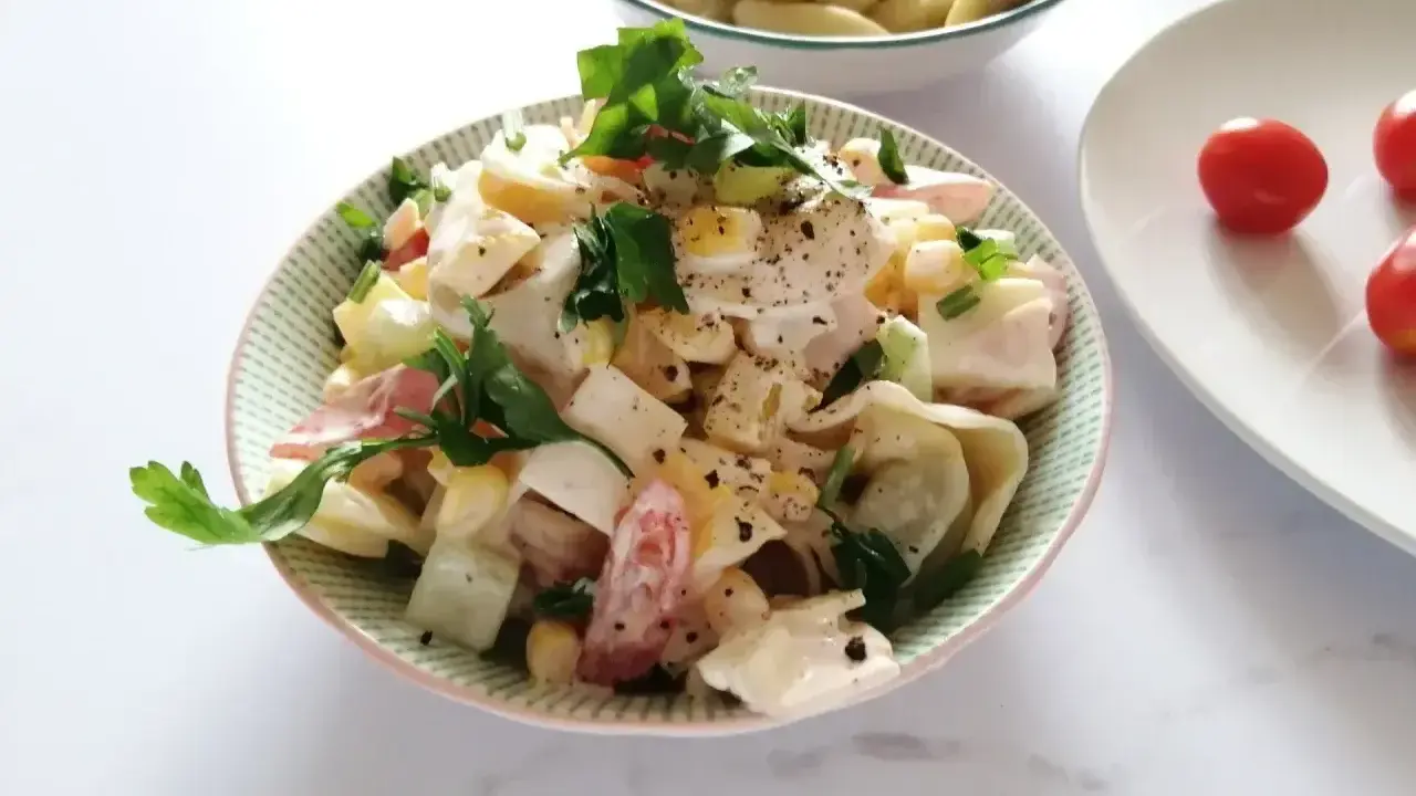 Pyszna sałatka z tortellini, jajka, kukurydzy i pomidorów, udekorowana natką pietruszki. Idealna na letnie dni.