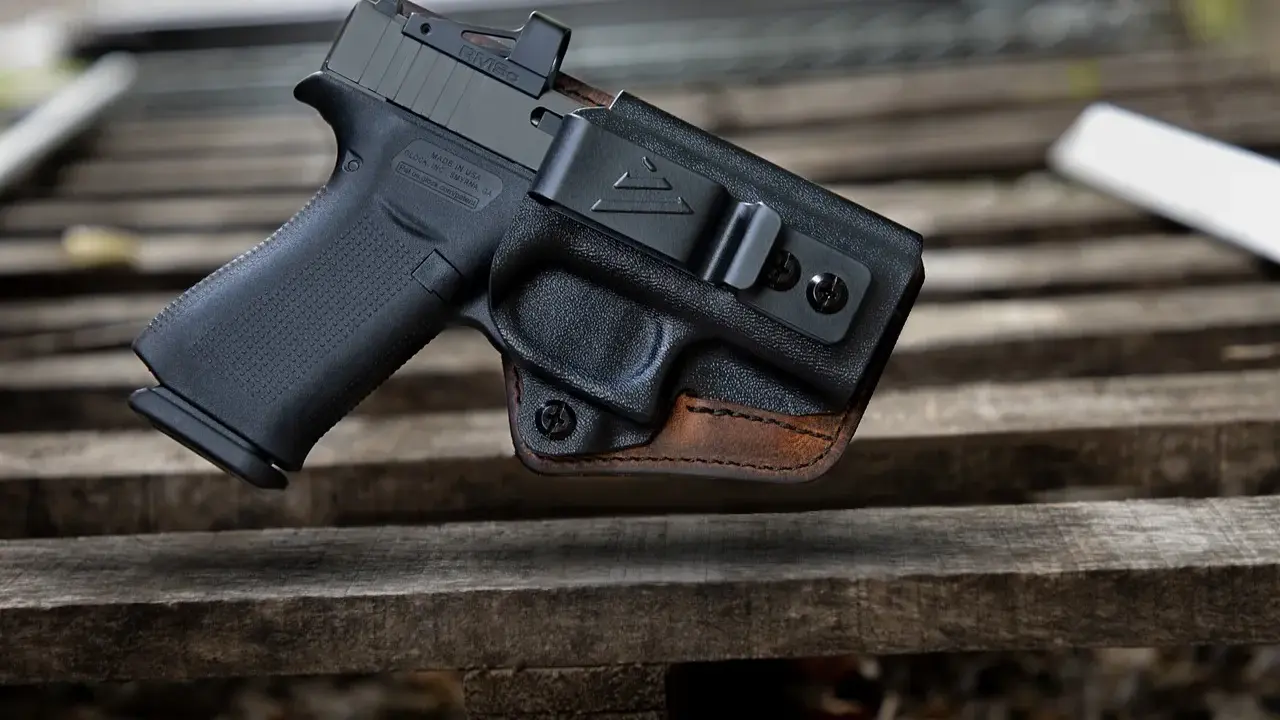 Pistolet w kaburze udowej z czarnego polimeru i brązowej skóry, z widocznym celownikiem optycznym.