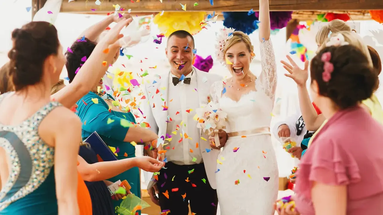 Glückliches Brautpaar im Konfettiregen, eine wunderschöne Tradition zur Hochzeit. Gäste werfen bunte Papierstreifen.