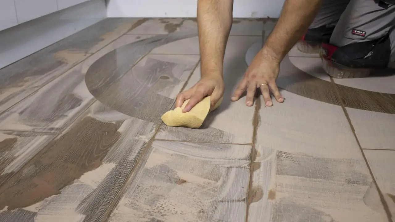 Man limpiando suelo porcelánico con una esponja. El suelo tiene un diseño de madera y un patrón curvo.