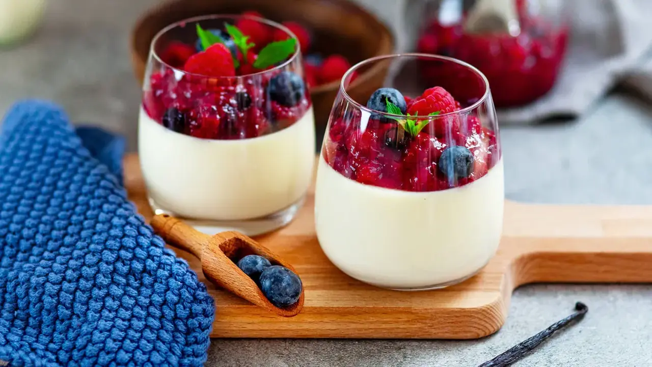 Zwei Gläser mit cremigem Panna Cotta, garniert mit Beeren und Minze. Ein köstliches Rezept für original italienische Panna Cotta.