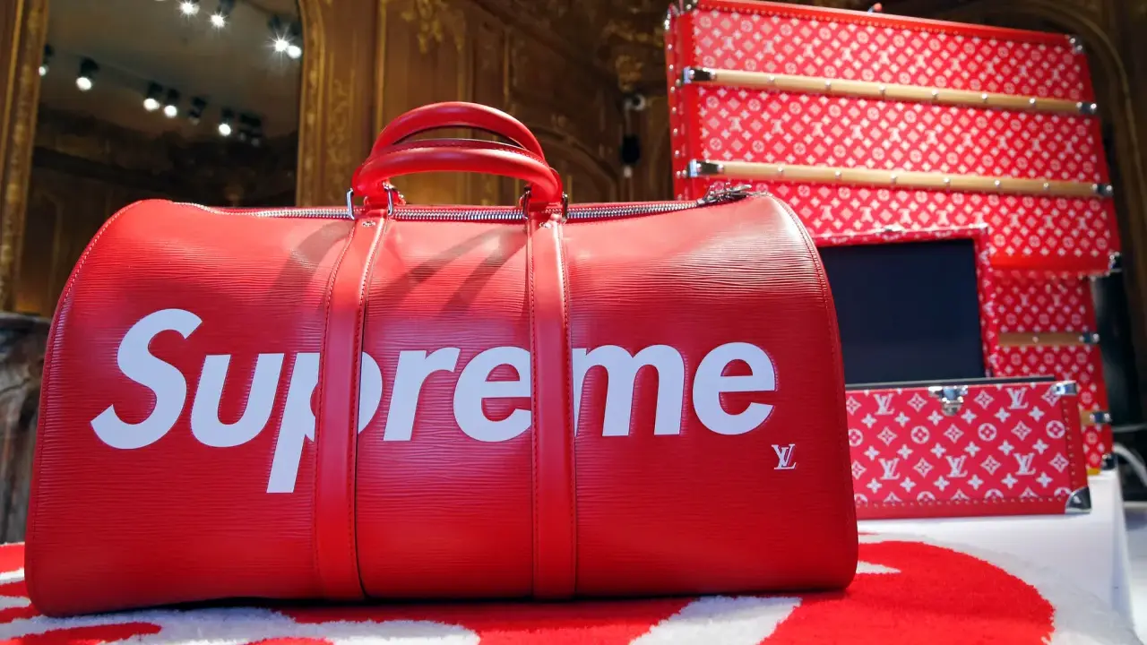 Czerwona torba podróżna z białym logo Supreme. Supreme to marka znana z limitowanych kolekcji i kolaboracji, jak ta z Louis Vuitton.