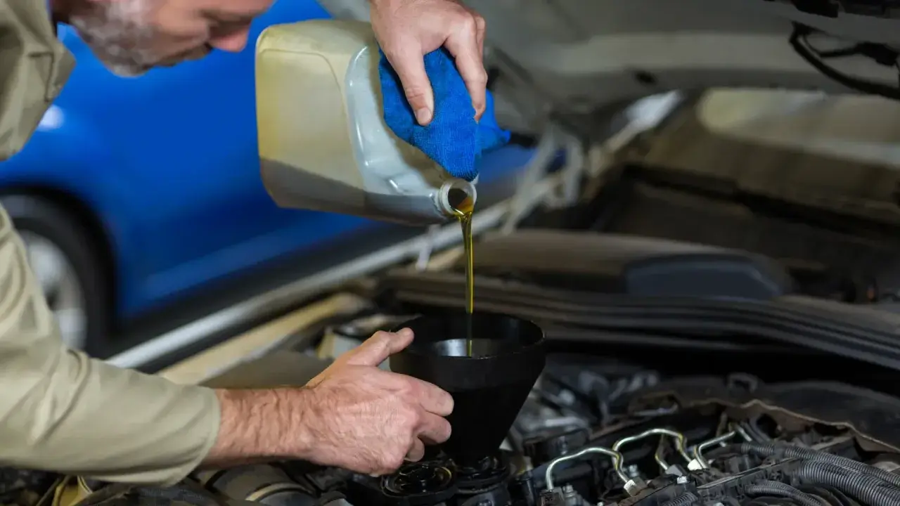 Mecánico vertiendo aceite nuevo en el motor para el mantenimiento del coche.