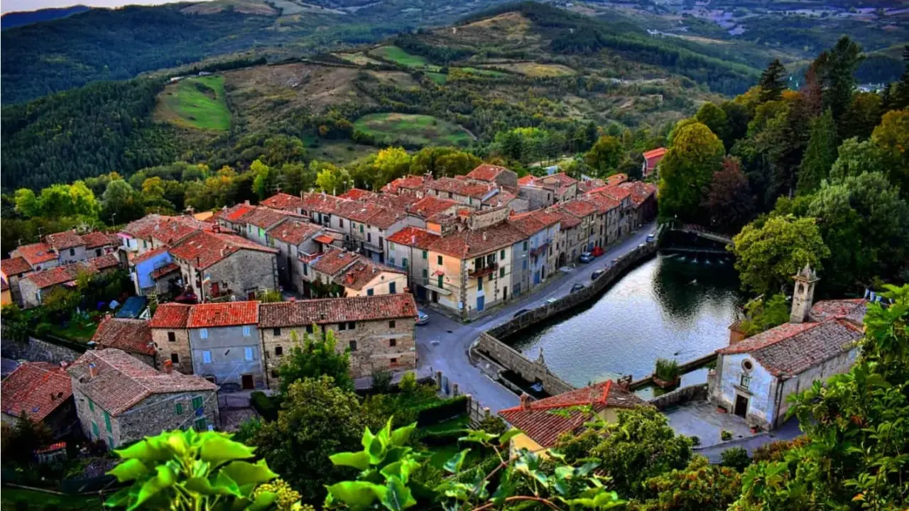 Vista aerea di Santa Fiora, con case dai tetti rossi che si affacciano su un laghetto e colline verdi sullo sfondo.