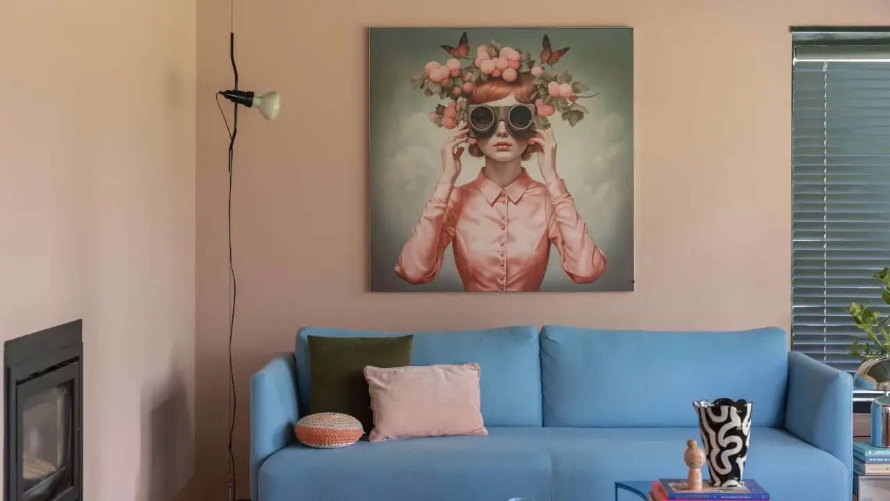 Ein hellblaues Sofa mit Kissen vor einem Bild, das eine Frau mit Blumenkranz und Schmetterlingen zeigt. Ein Beispiel für die Wohntrends 2026.