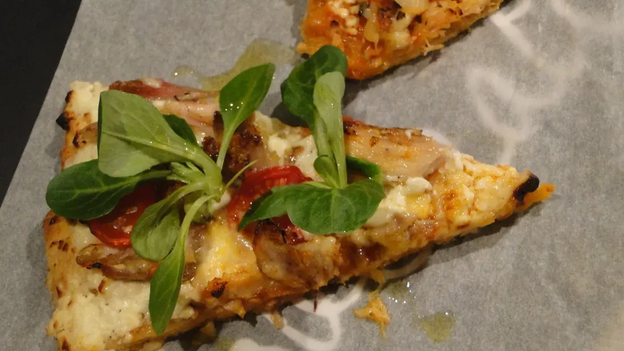Dwie porcje pizzy z twarogu, z pomidorkami i świeżymi ziołami, na papierze do pieczenia.