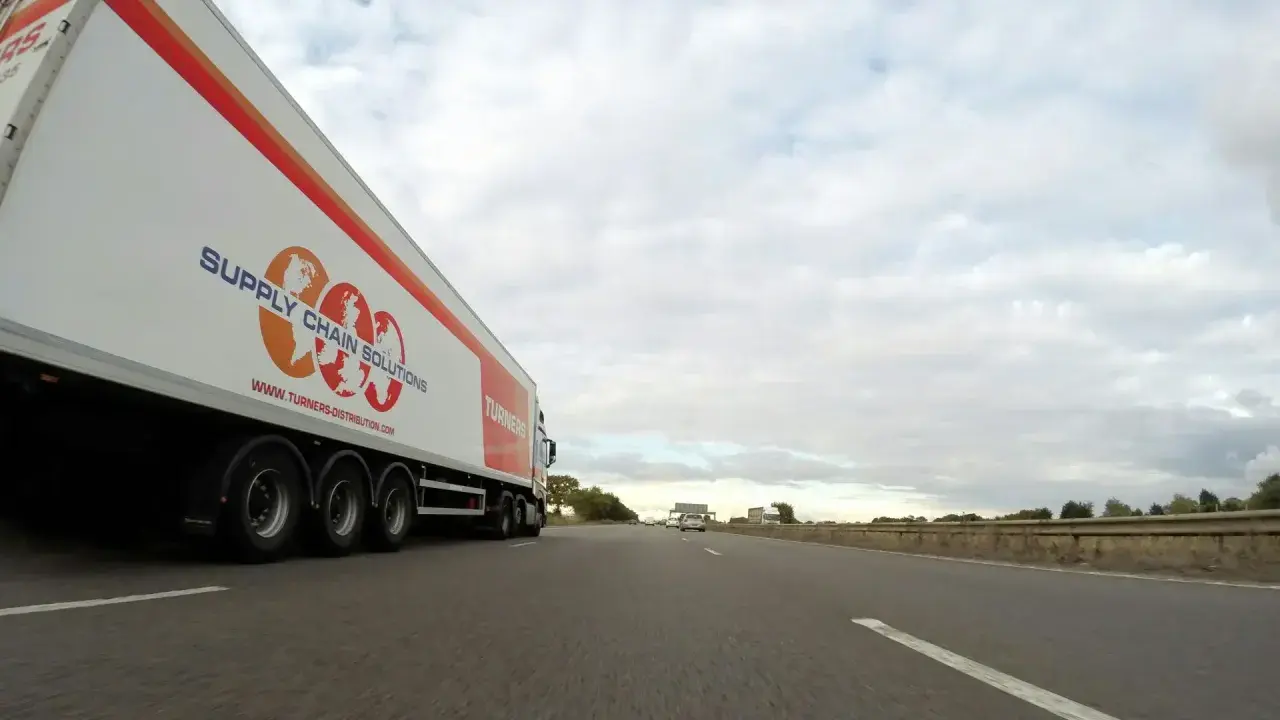 Camión de carga con el logo "Supply Chain Solutions" y "Turners" avanza por la autopista.