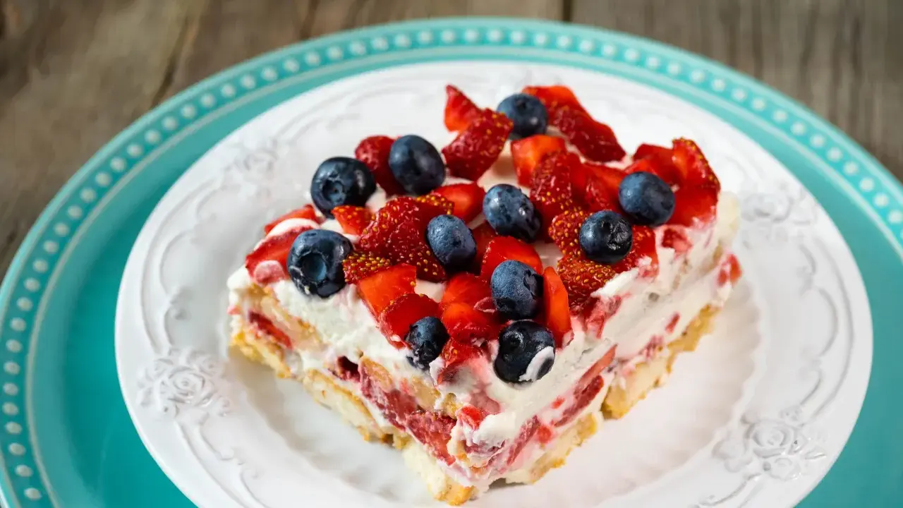 Tranche de tiramisu aux fruits rouges, garnie de fraises et myrtilles fraîches. Un délice estival.