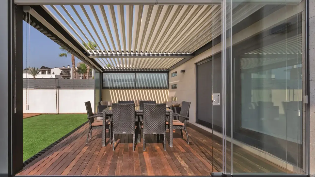 Porches cerrados con encanto, con mesa y sillas de mimbre sobre tarima de madera y césped artificial.