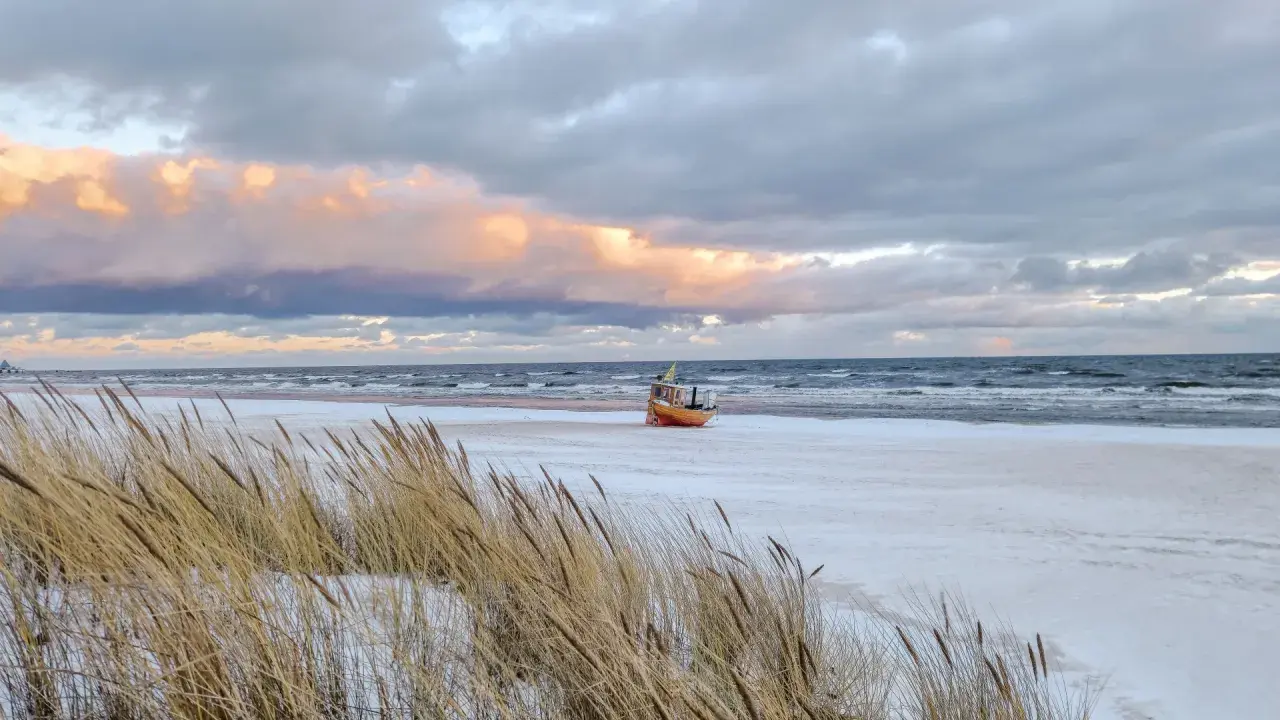 Ein kleines Boot liegt am verschneiten Strand der Ostsee, im Hintergrund die Seebrücke von Ahlbeck.