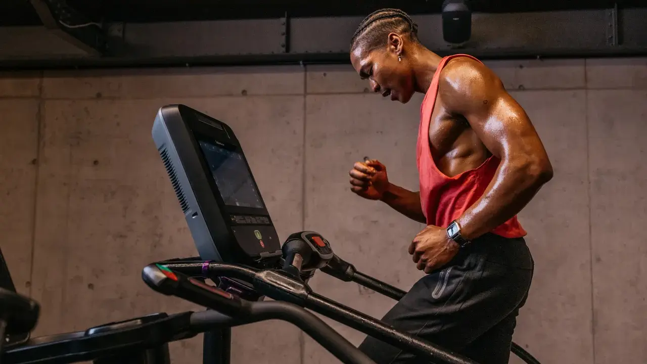 Schwitzender Mann im roten Tanktop läuft auf Laufband. Perfektes Cardio nach dem Krafttraining.