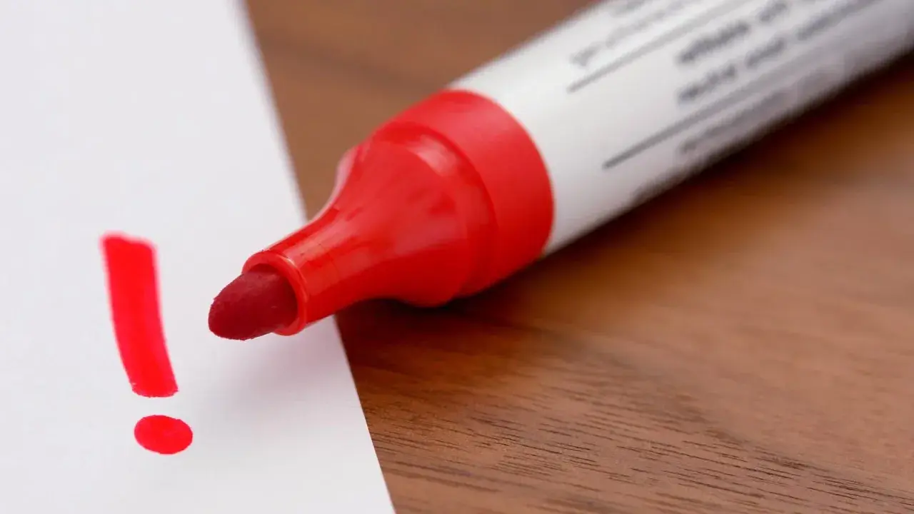 Roter Filzstift schreibt ein Ausrufezeichen auf weißes Papier. Ein wichtiger Hinweis, der sich leicht vom Filzstift von Haut entfernen lässt.