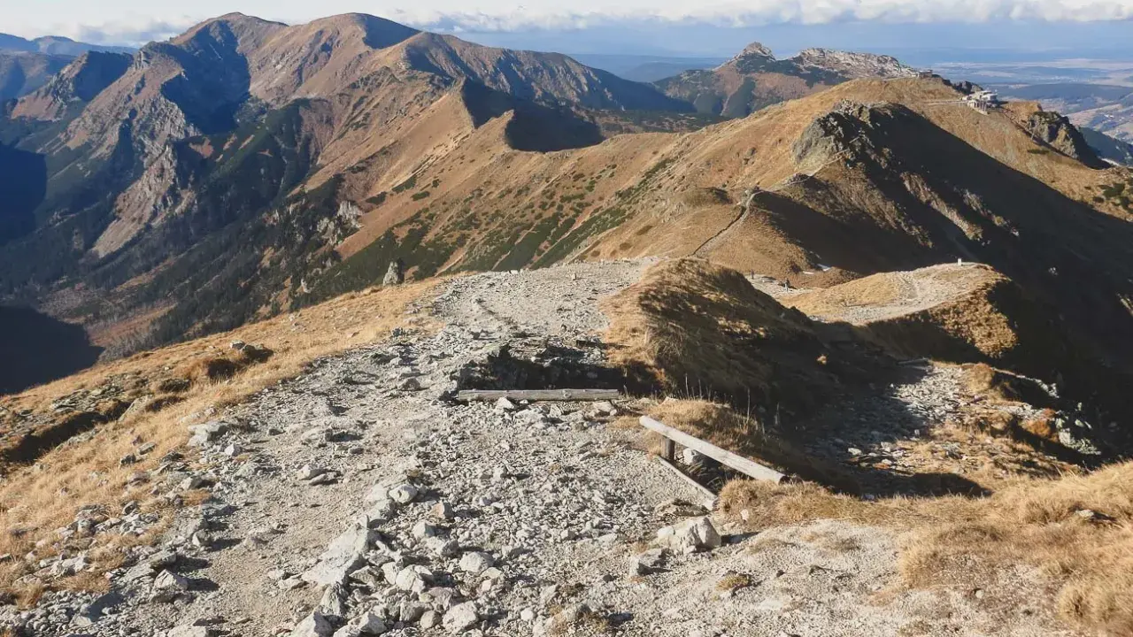 Kamienista ścieżka prowadzi przez trawiaste zbocza, ukazując najpiękniejsze doliny Zakopane. W oddali majaczą góry.
