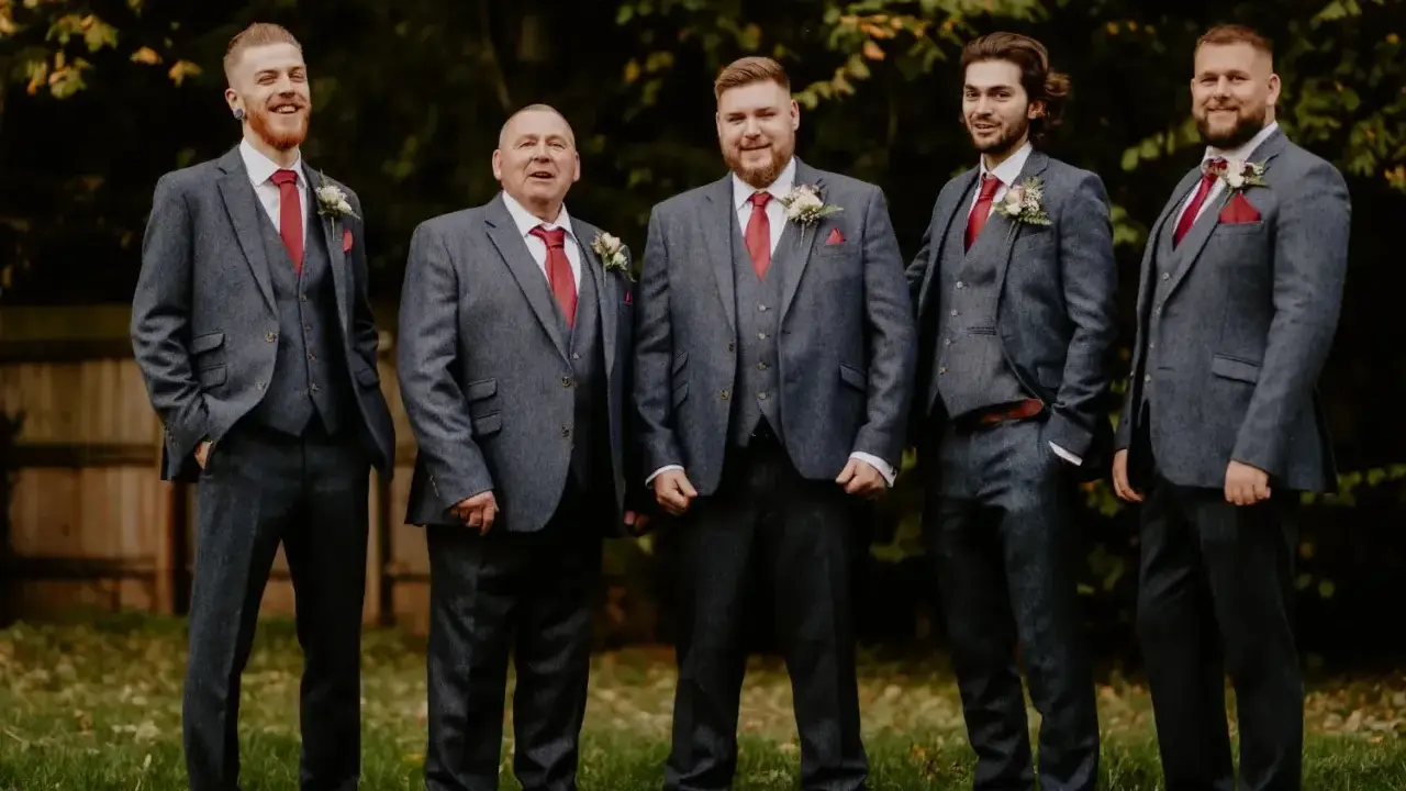 Five men in matching grey suits with red ties and pocket squares. The price of tuxedos can vary, but these look like a good investment for a wedding party.