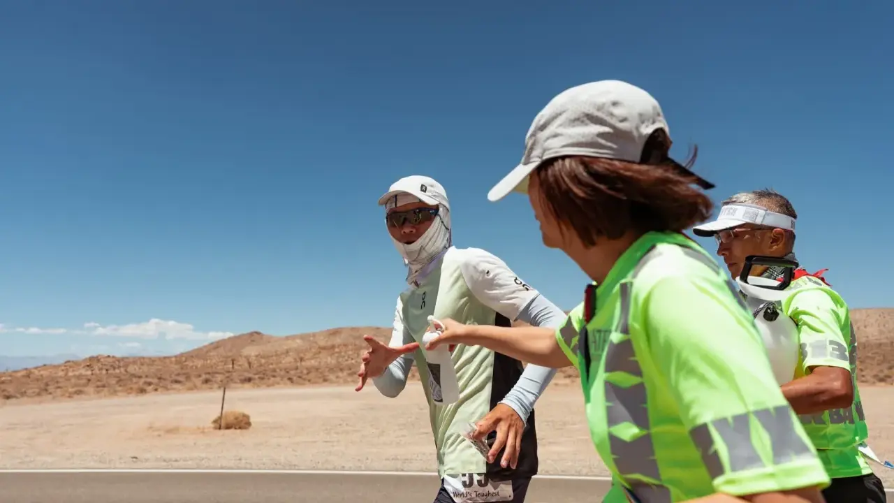 Läufer beim Badwater 135 Ultra-Marathon in der Wüste. Eine Helferin reicht einem Läufer Wasser.