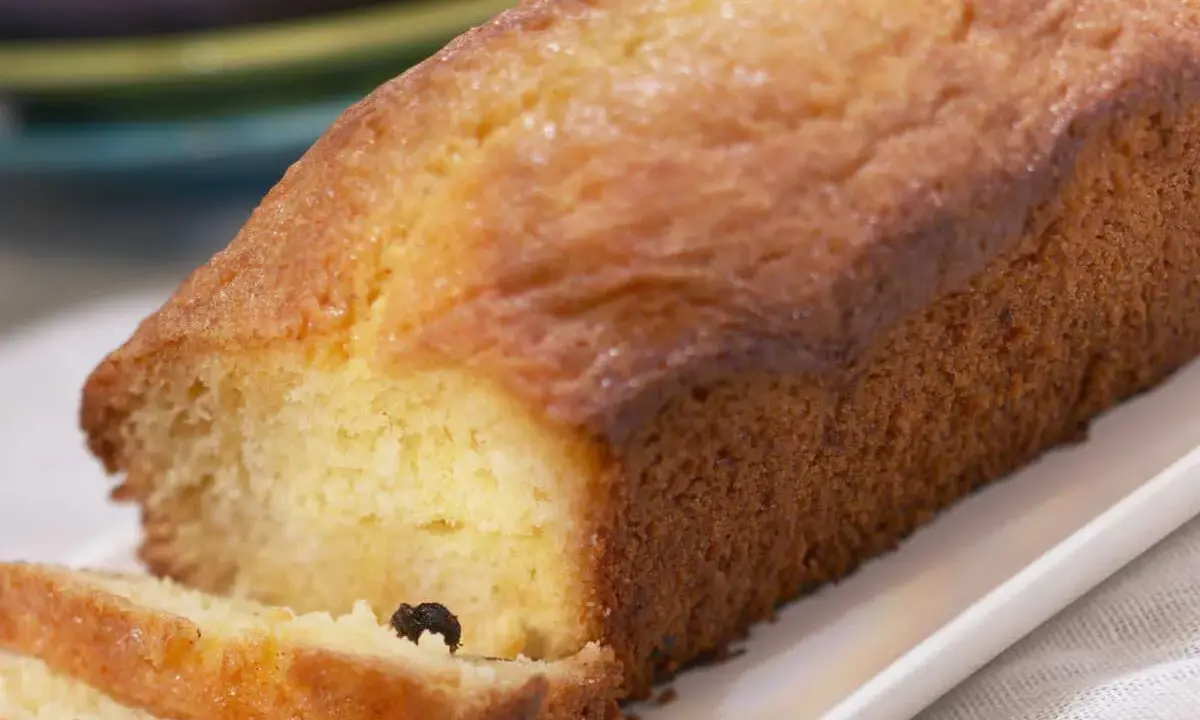 Un cake doré, parfait pour une recette facile. Deux tranches sont coupées, révélant une mie moelleuse et quelques raisins secs.