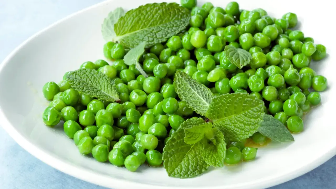 Petits pois frais et menthe sur une assiette blanche, une idée simple pour une recette de petit pois légère et savoureuse.