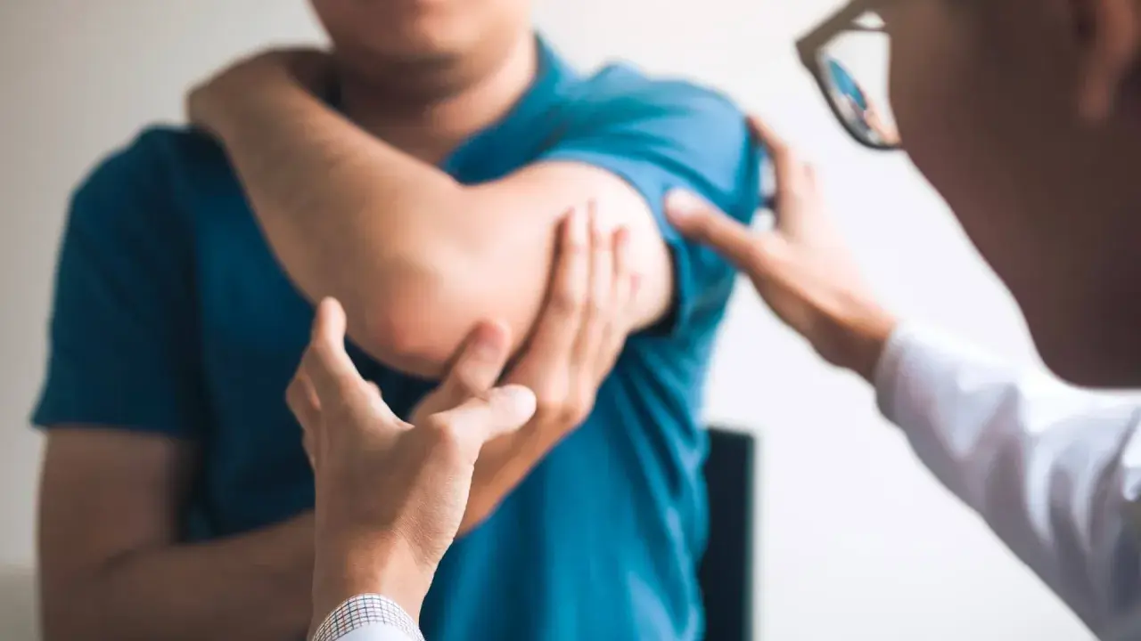 Un médecin examine le coude d'un patient, possiblement atteint du syndrome de la souris, une maladie professionnelle liée à l'usage intensif de l'ordinateur.