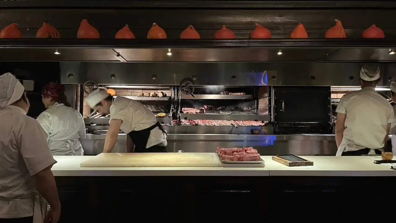 Chefs preparan cortes de carne en la parrilla Don Julio, con brasas ardientes y un ambiente de cocina profesional.