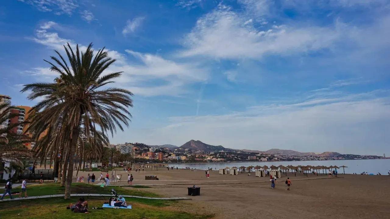 Sonniger Strand an der Costa del Sol mit Palmen, Menschen und dem Meer im Hintergrund.