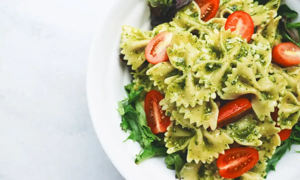 Pyszna sałatka z makaronem farfalle w sosie pesto, z pomidorkami koktajlowymi i świeżą sałatą.