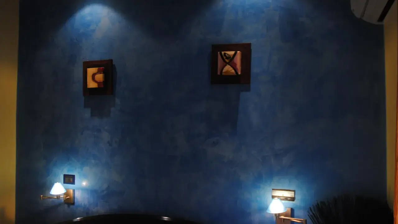 Pared azul con efecto veladura, dos cuadros abstractos y lámparas de pared.