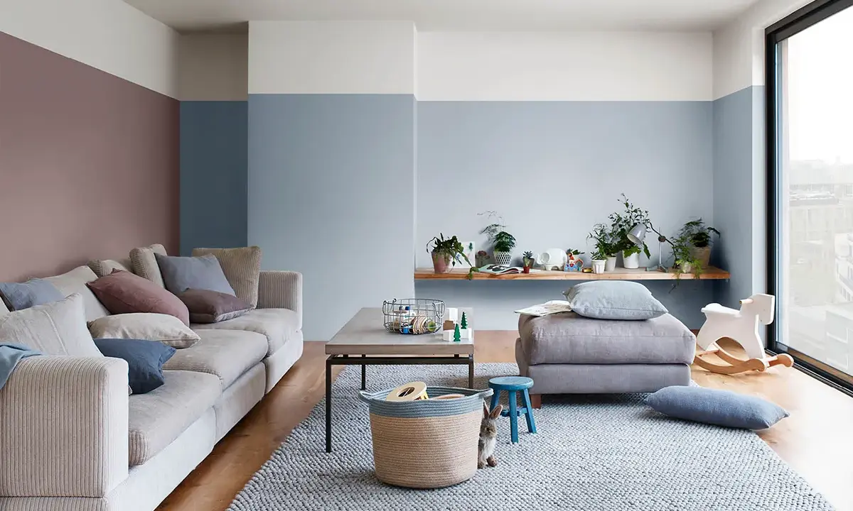 Soggiorno accogliente con divano beige, tappeto grigio e pareti color carta da zucchero. Un coniglietto curioso osserva dal cesto.