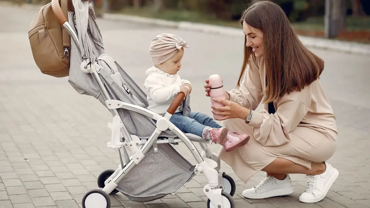 Mama karmi córeczkę z butelki, siedząc obok wózka. Idealne wózki dla dziewczynki na spacer.