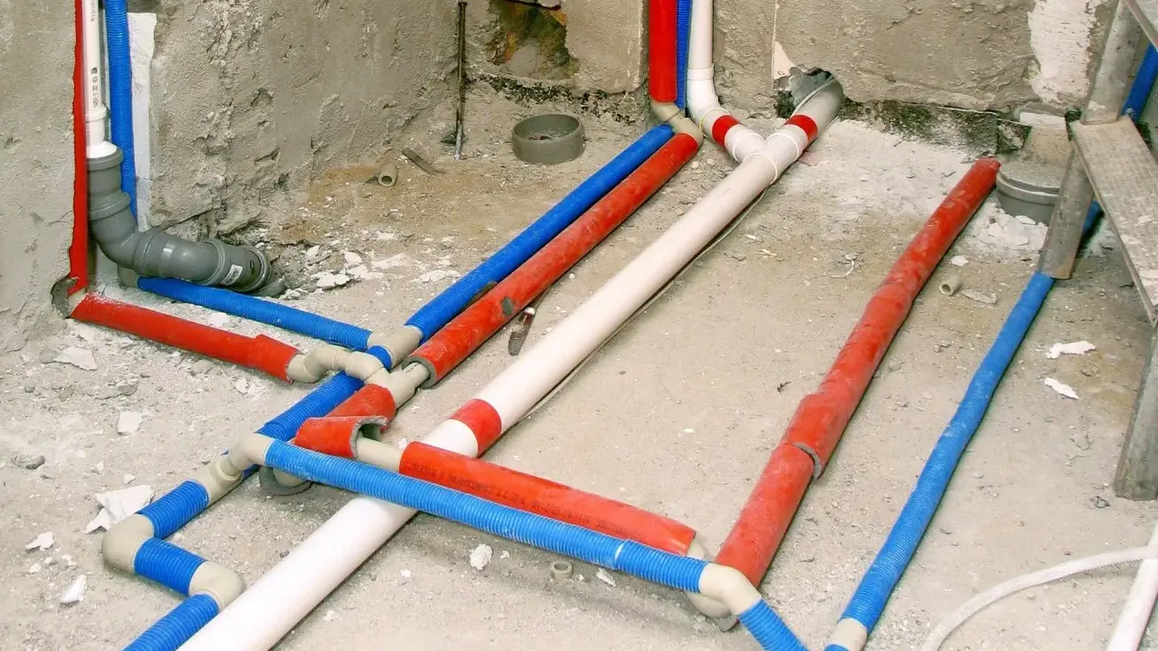 Skomplikowana instalacja wodociągowa z rurami w kolorach czerwonym, niebieskim i białym, przygotowana do ukrycia w ścianie.
