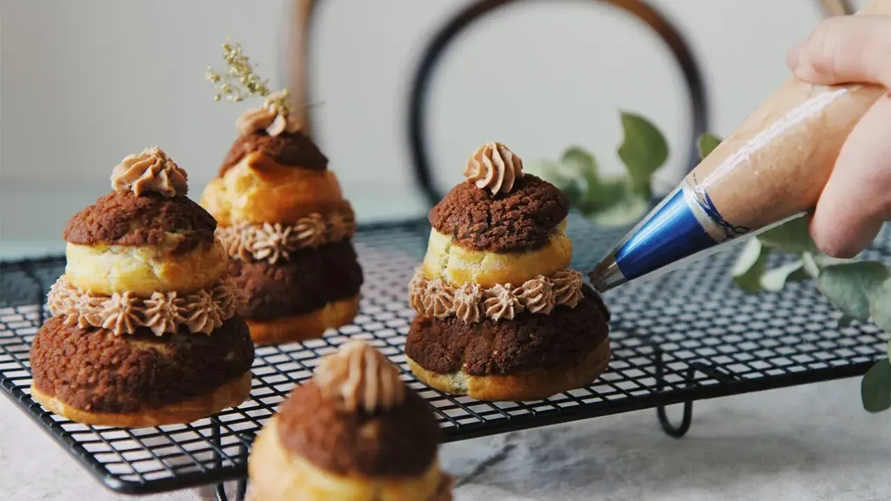 Finition d'une religieuse au chocolat avec une touche de crème. Ces pâtisseries sont prêtes à être dégustées.