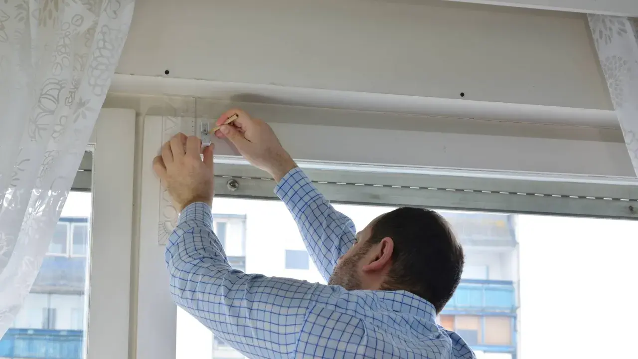 Hombre con camisa a cuadros midiendo para reparar persianas.