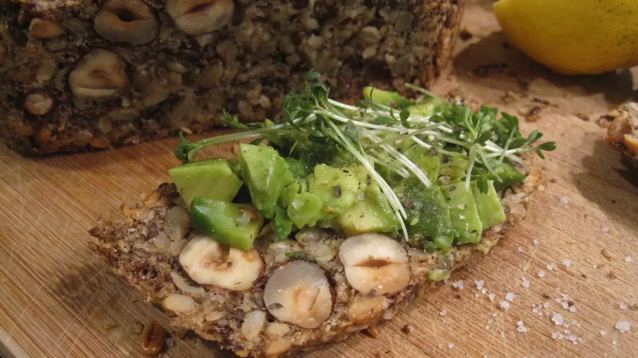 Ein Stück herzhaftes Flohsamenschalen Brot mit Nüssen, belegt mit Avocado und Kresse. Ein gesunder Genuss!