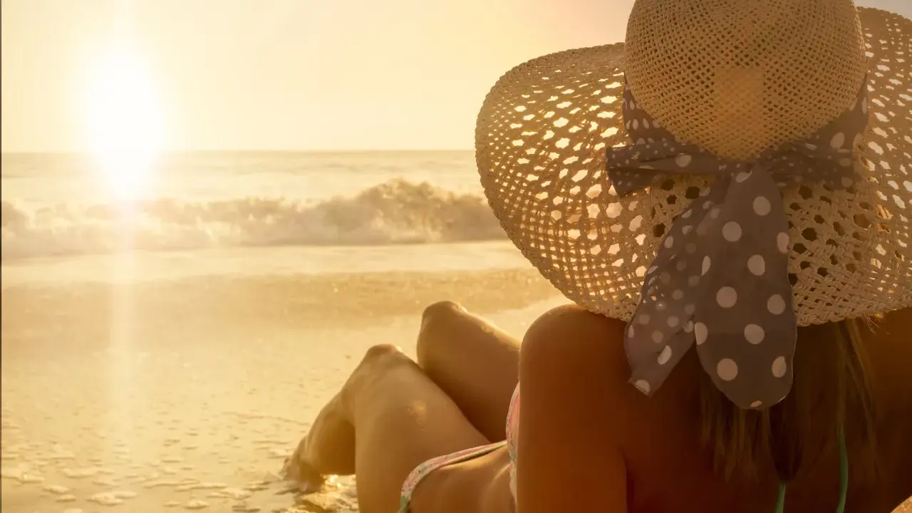 Donna con cappello di paglia e un bikini a pois, godendosi il tramonto sulla spiaggia. La sua pelle ha una perfetta abbronzatura arancione.