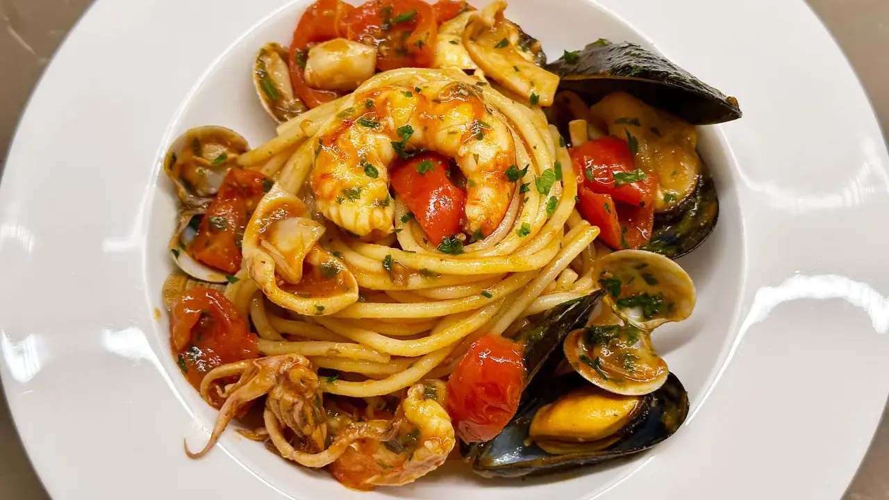 Spaghetti allo scoglio with shrimp, mussels, clams, squid, and cherry tomatoes in a white bowl.